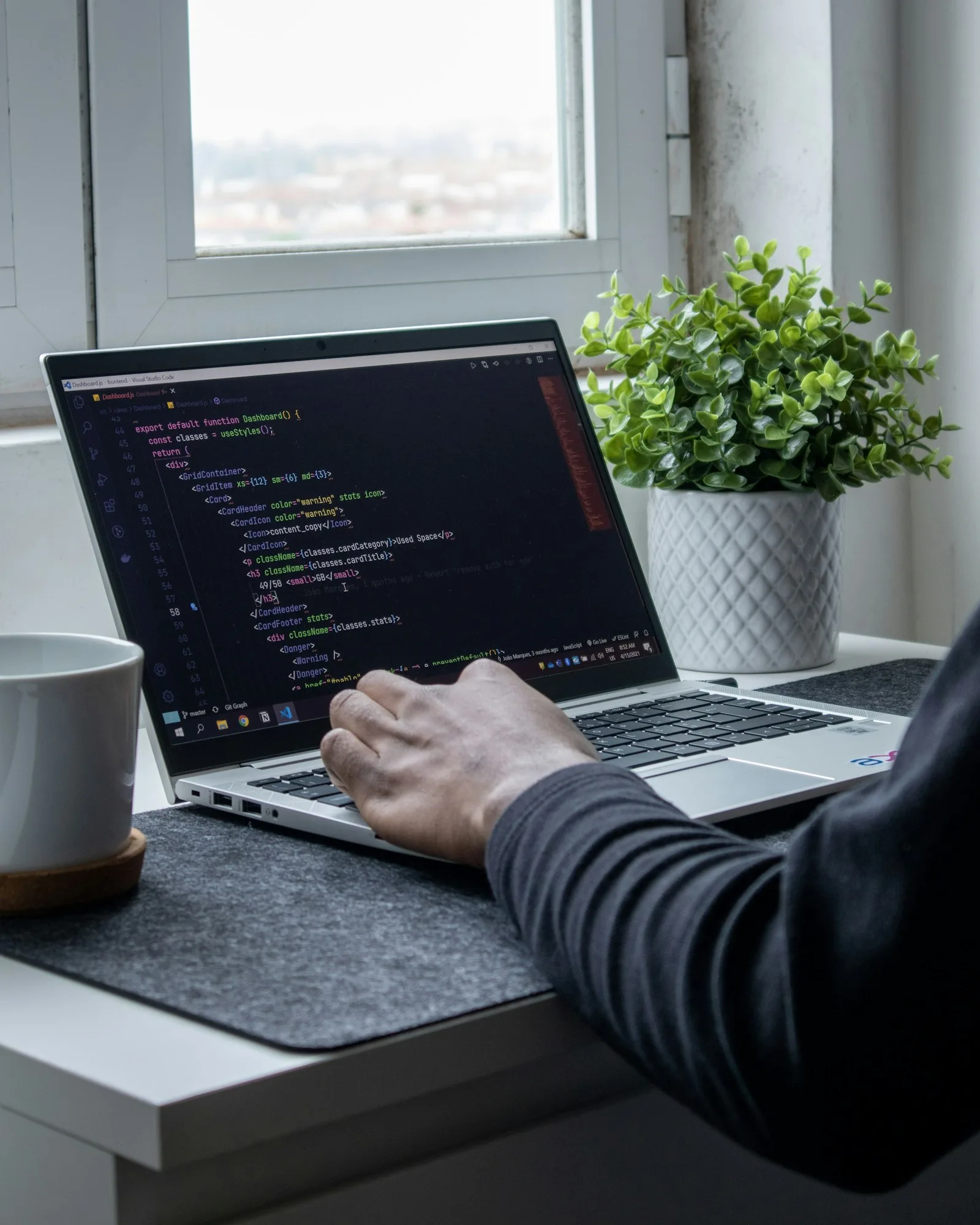 Developer typing code on a laptop beside a plant and a mug