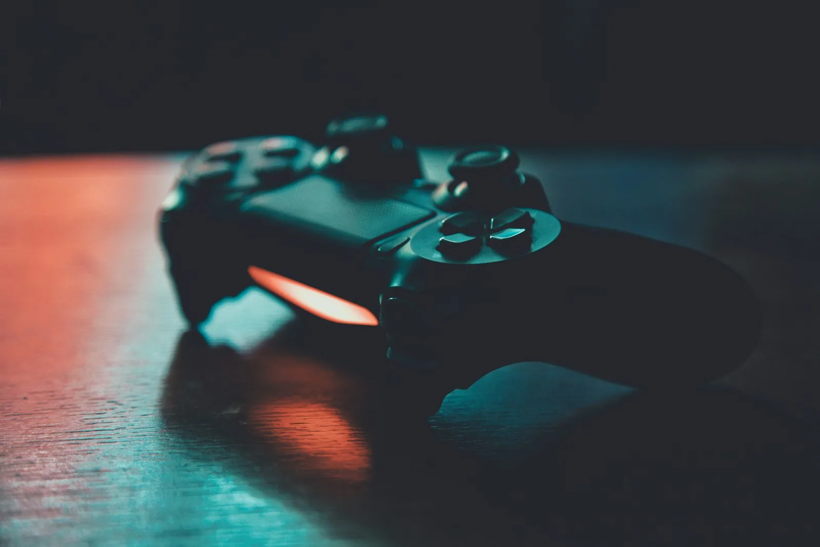 Black game controller on a wooden surface with blue and orange lighting